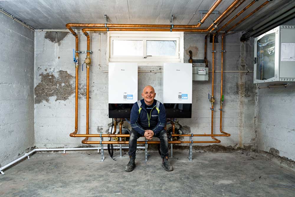 VVS-service person sitter och tittar in i kameran mellan två luft/luft värmepannor. Trelleborgs Rörservice personal. Rörläggare, VVS 